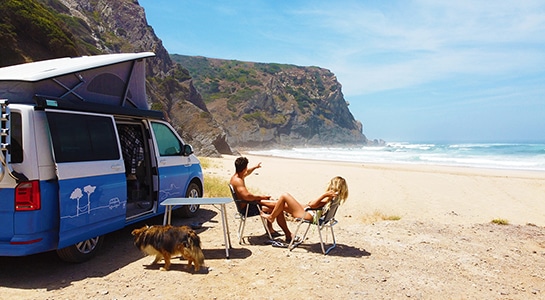 couple sitting on chairs at the beach in front of a camper