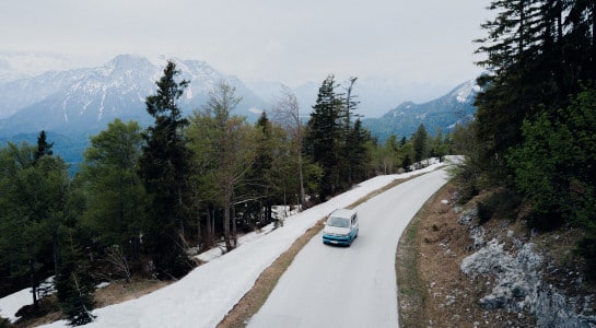 campervan driving on a snow covered road, mountains in the background