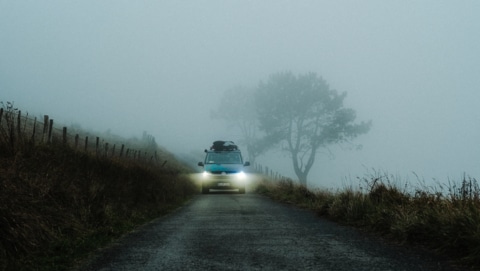 Campervan driving through fog with headlights on.