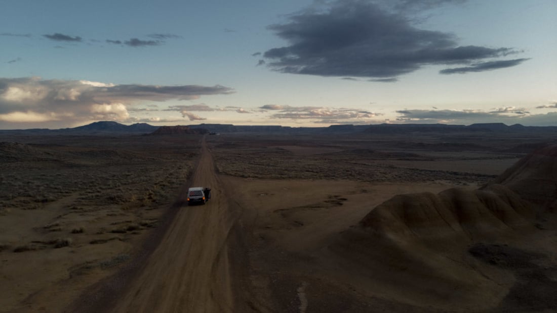 a campervan on a road through the desert, sunset