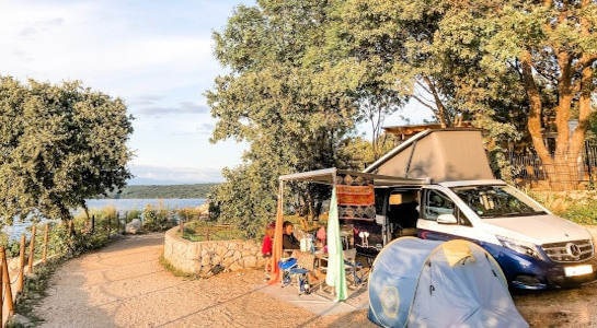 a campsite with a van and tent by a lake