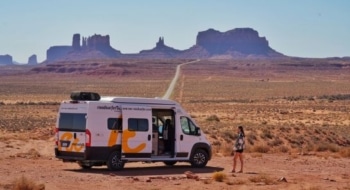 Camper van parked on a desert road in Monument Valley with rock formations in the background