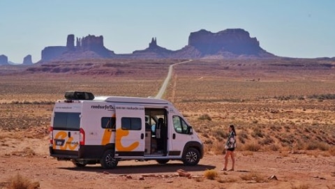 Camper van parked on a desert road in Monument Valley with rock formations in the background