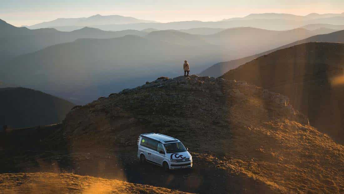 campervan on a hill with mountain view, person standing on the top of a hill