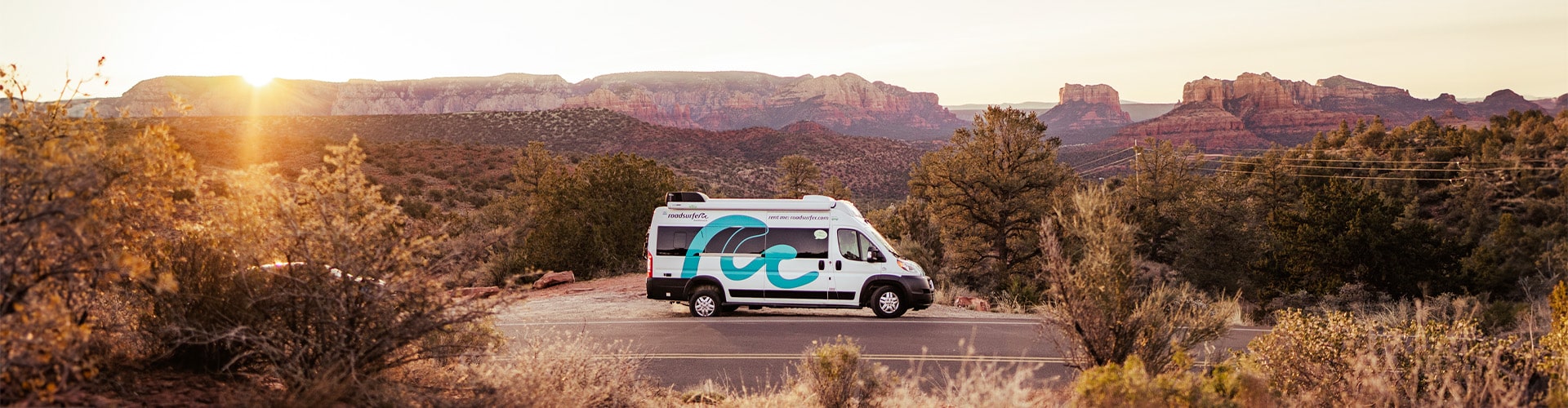 A campervan parked next to the road on graveled ground at sunset with stone mountains in the background