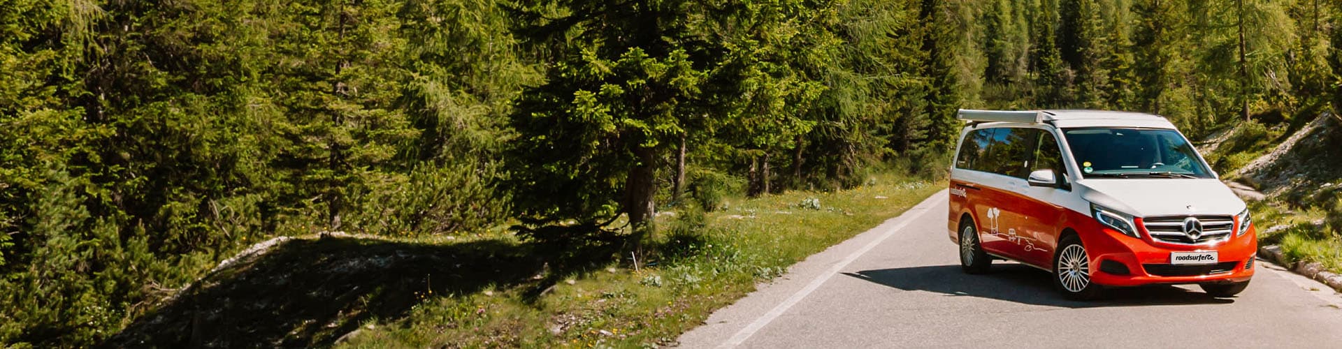 Red Mercedes Marco Polo Campervan parked on a road next to a forest on a sunny day