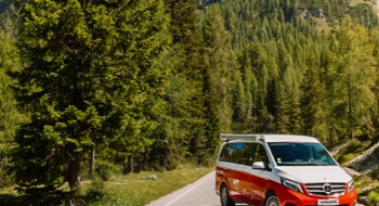 Red Mercedes Marco Polo campervan parked on a road next to a forest on a sunny day