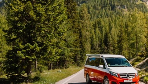 Red Mercedes Marco Polo campervan parked on a road next to a forest on a sunny day