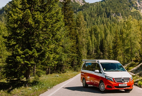 Red Mercedes Marco Polo campervan parked on a road next to a forest on a sunny day