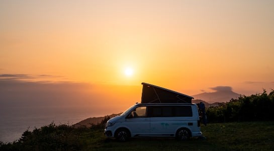 campervan with open roof parked near a cliff at sunset