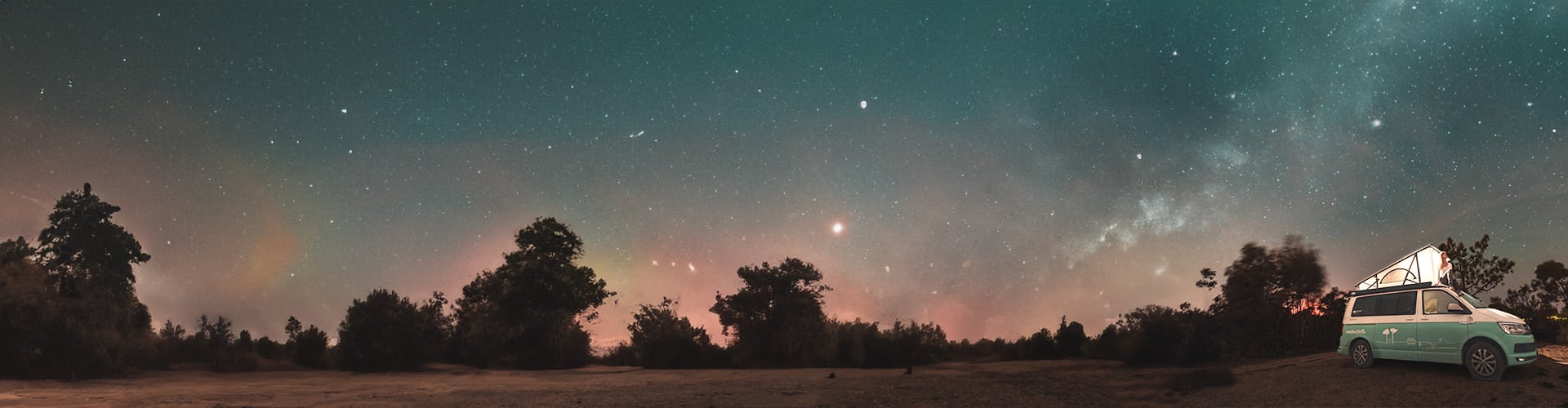 campervan with opened pop up roof parked underneath starry sky