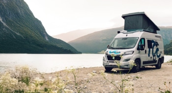 camper van with a pop-up roof parked by a scenic lake, surrounded by mountains and lush greenery, creating a tranquil outdoor setting