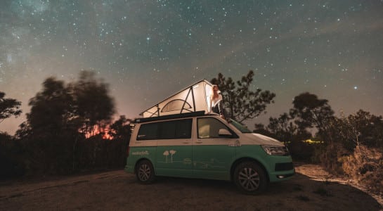 girl sitting in the pop up roof of a campervan under the stars