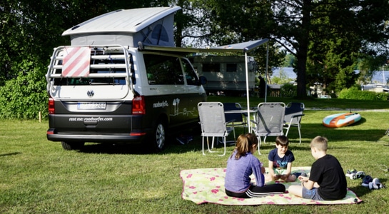 Three children sitting and playing on a field with a campervan in the back