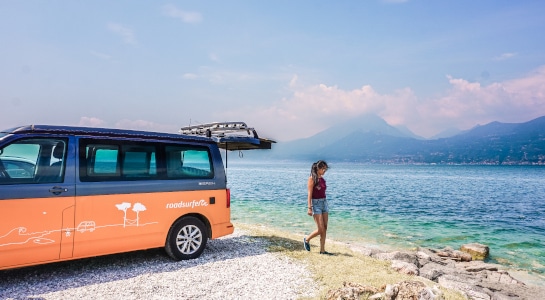 Orange VW camper in front of the sea with girl walking into the water
