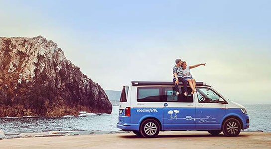 couple sitting on a vw van at the beach