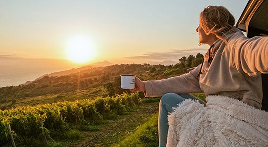 roadsurfer spots campsite at a vineyard in France, with a girl drinking coffee at sunrise in the foreground
