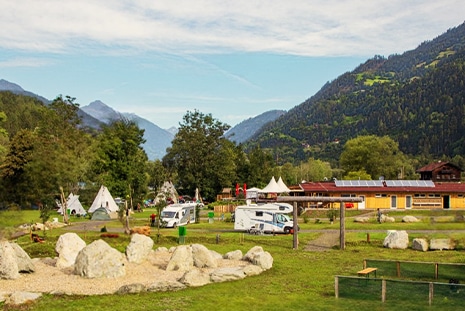 Campervans can be seen standing on a campsite in Austria with the view over the Dolomites Mountains on a sunny day.