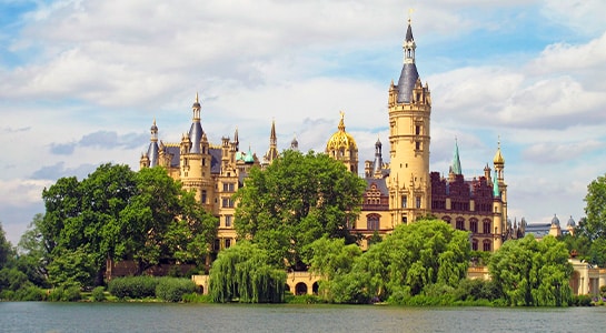 Big castle in Schwerin visible from the waterfront and built behind trees.