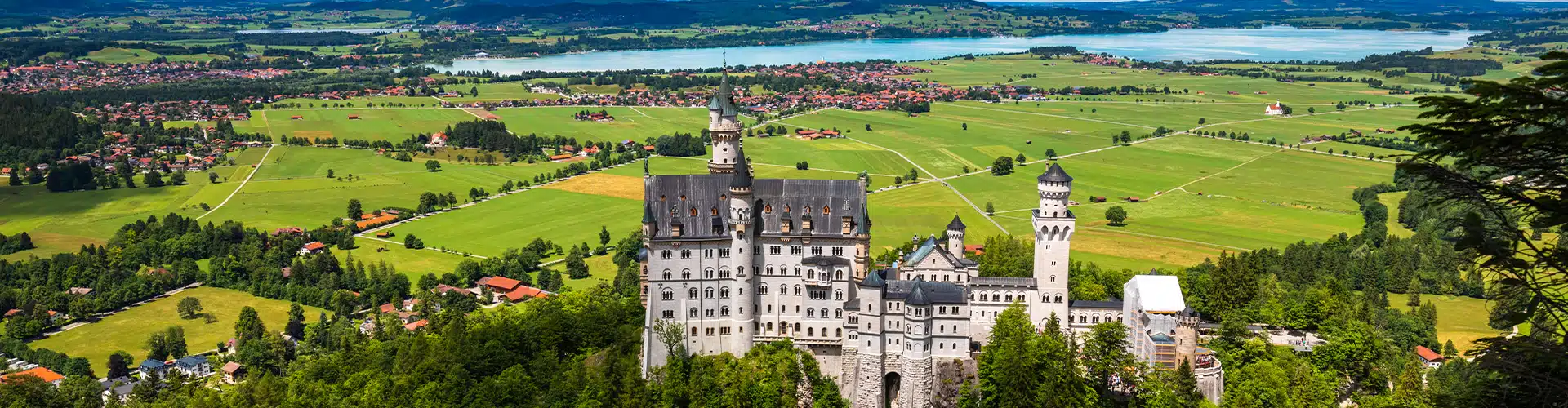 Castle Neuschwanstein in Germany situation on a hill with a view over the valley and a lake in the far back.