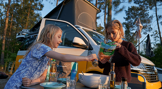 Two children preparing the dinner table outside of a yellow roadsurfer campervan