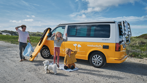 Children are playing with their father and dog around a yellow camper.