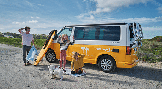 Children are playing with their father and dog around a yellow camper.