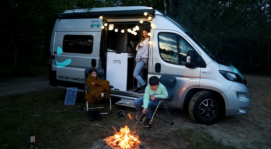children sitting around the campfire, mom in the camper van