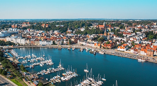 City of Flensburg photographed from above with sailboats, river and city panorama visible.