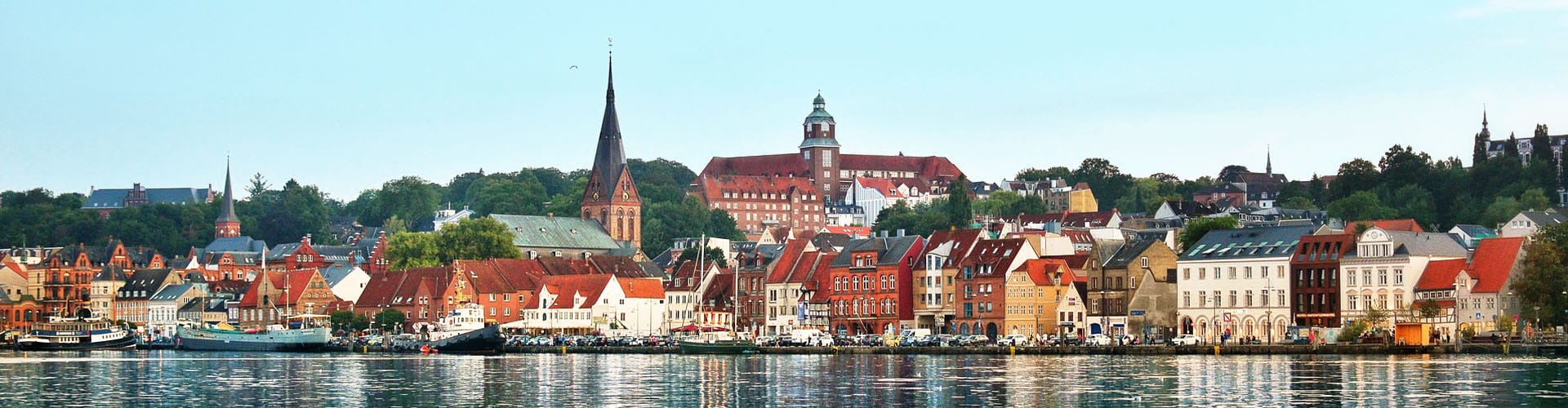 City of Flensburg photographed from the riverside with view over the boats, promenade and colorful houses.