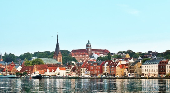 City of Flensburg photographed from the riverside with view over the boats, promenade and colorful houses.