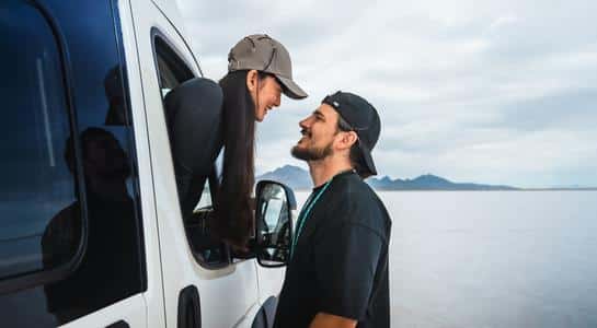 Two travelers sharing a moment outside their Class B RV rental parked on wide open salt flats.