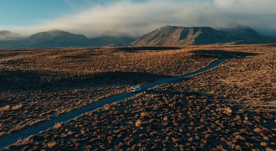 Class B RV rental driving along a remote desert road with mountains in the distance.