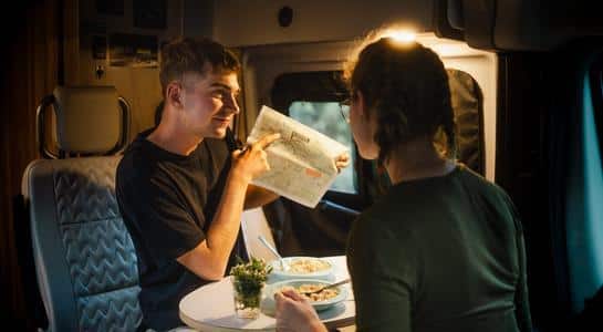 Couple reviewing a map inside their Class B RV rental while eating at the dining table