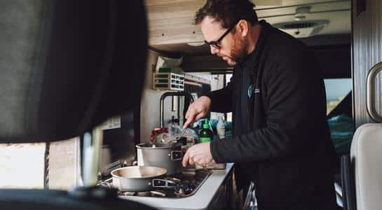 Man preparing a meal inside the compact kitchen of a Class B RV rental.
