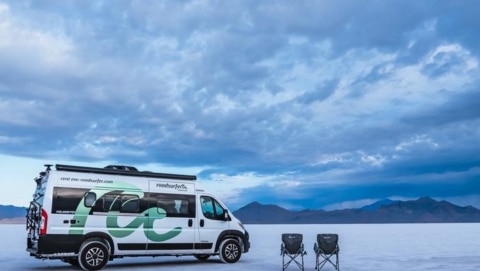 Class B RV rental parked on the salt flats with two camping chairs and mountains in the distance