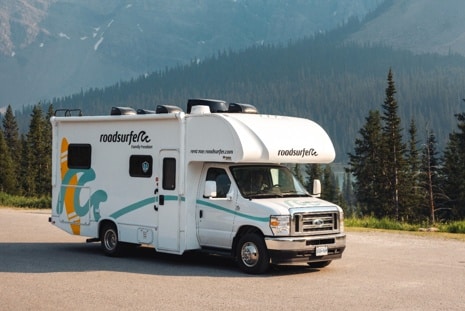 A white roadsurfer Class C RV parked on a mountain road beneath towering peaks, illustrating the appeal of Class C RVs for mountain road trips.
