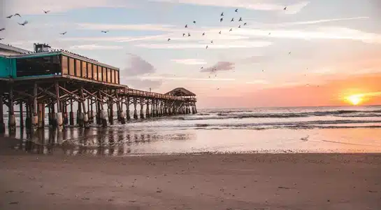 Cocoa Beach Pier extending over the ocean with birds flying at sunset in Cape Canaveral, Florida.