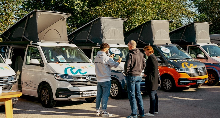 Consultation conversation between a couple and a roadsurfer employee on a sales day in front of campervans with opened pop up roofs