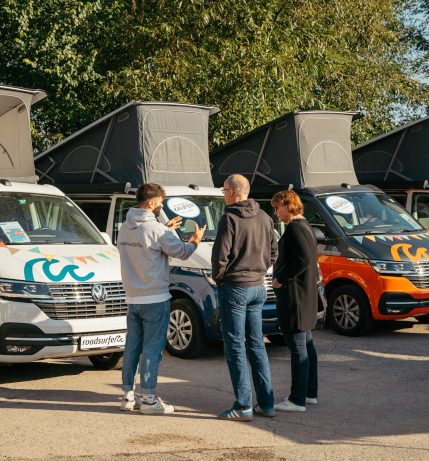 Consultation conversation between a couple and a roadsurfer employee on a sales day in front of campervans with opened pop up roofs