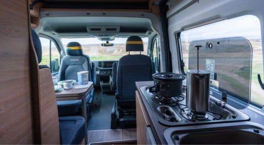 Interior layout of a conversion van showing the kitchen, dining area, and front seats