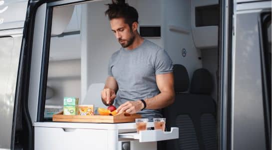 Traveler preparing food inside a conversion van kitchen during a road trip