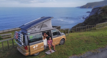 Couple sitting in a campervan next to a cliff with views on the coast