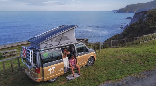Couple sitting in a campervan next to a cliff with views on the coast