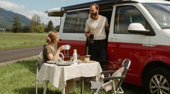 Couple having breakfast outside of their red campervan