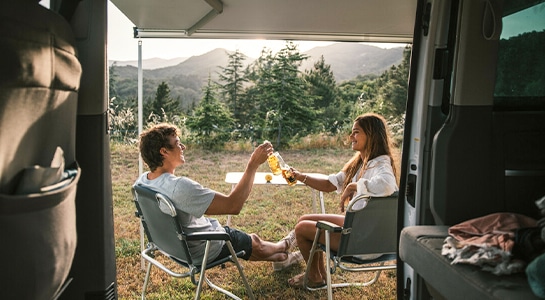 couple having a drink in summer in front of a camper van