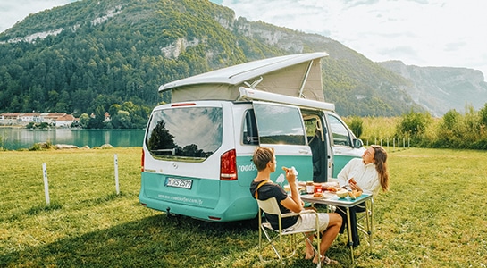 couple having breakfast next to a campervan in front of a lake