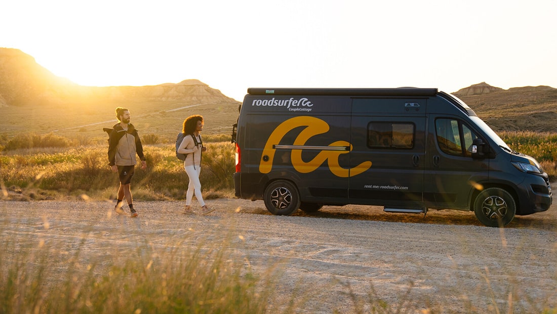 Couple with backpacks hiking next to a campervan at sunset