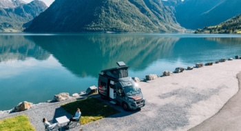 Boxvan parked at the lakeside and a couple sitting around a camping table.