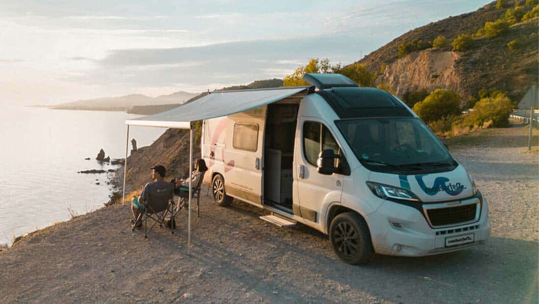 Couple sitting in front of a campervan at the cliffs enjoying the view and the sunset